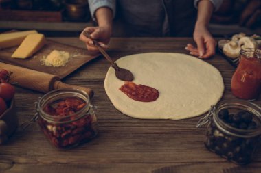 Pizza yapma süreci. Hamur el Tepesi hazırlayın. Kadın el pastörize domates salçası bir pizza tabanı üzerine yayılıyor. Gıda kavramı. Geleneksel İtalyan pizza hazırlanıyor. Tonlu görüntü.