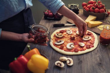 Ellerini pişir. Ellere yakın, masanın etrafında bazı malzemeler. Taze orijinal İtalyan çiğ pizza, geleneksel tarzda hazırlık. Malzemeler ve baharatlar ahşap masada ev yapımı pizza yapmak için.