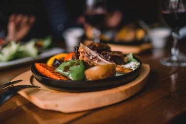 Yemek ve eğlence kavramı. Yemek masada. Sebze ve otlar bir kavurma demir Pan ile lezzetli ızgara kuzu bacak. Çeşitli lezzetli sebze ızgara et ile. Tonlu görüntü. Seçici odak