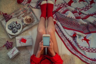 Woman using smartphone for browsing internet store at home. Online shopping conceptspace for text. Mood winter. Seasonal holidays. Merry Christmas and New Year. Top view. Toned image. Selective focus.