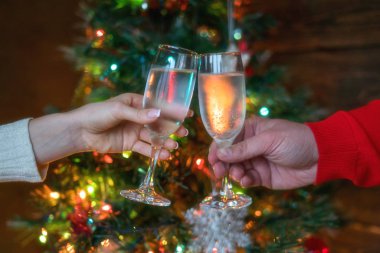 Şerefe! Womam ve adam arka planda Noel iç şampanya flüt ile tezahürat. Tatil konsepti. Akşam ışıkları parlıyor. Yeni yıl kutlaması. Tonlu görüntü. Seçici odaklama.