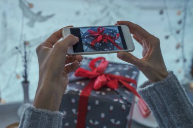 Genç bir kadın, blogcu Noel tatili için hazırlanıyor ve akıllı telefonda fotoğraf çekiyor. Sosyal ağlarda cep telefonu tutan ve sohbet eden bir kadının elleri. Görüntü tonlaması. Seçici odak.