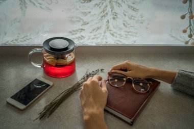 Su ısıtıcısı meyve çayı, kağıt defter, akıllı telefon ve gözlük taş masada kış penceresi önünde. Sabah planlaması ve meyve çayı ile ilham. Kış sıcak içeceği. Tonlu görüntü.