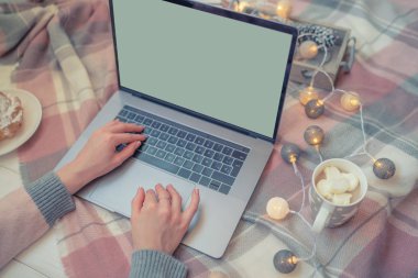 Noel'in tadını evde geçiriyorum. Evde bir katta otururken dizüstü bilgisayar üzerinde çalışan ve kahve içen genç kadın. Boş beyaz ekranlı dizüstü bilgisayarda kullanan ve yazan kızın üst görünümü mockup görüntüsü.