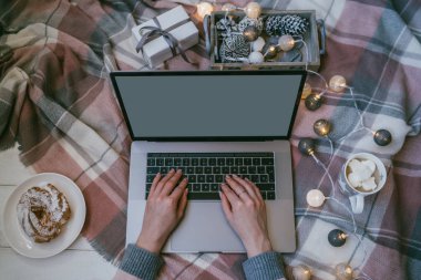 Noel'in tadını evde geçiriyorum. Evde bir katta otururken dizüstü bilgisayar üzerinde çalışan ve kahve içen genç kadın. Boş beyaz ekranlı dizüstü bilgisayarda kullanan ve yazan kızın üst görünümü mockup görüntüsü.