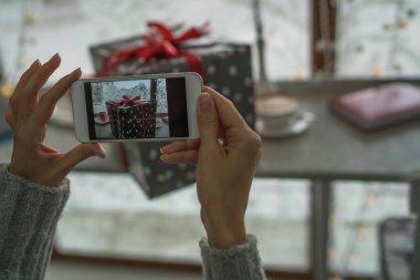 Genç bir kadın, blogcu Noel tatili için hazırlanıyor ve akıllı telefonda fotoğraf çekiyor. Sosyal ağlarda cep telefonu tutan ve sohbet eden bir kadının elleri. Görüntü tonlaması. Seçici odak.