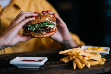 Lezzetli ızgara sığır eti, domates, peynir, salatalık ve marul ile burger yaptı. Kadın elinde burger tutar.