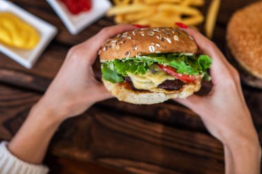 Çizburger tutan kadın. El ele tutuşan genç bir kız fast food burger, Amerikan yemeği. Köy tahtasında patates kızartması ve sığır burger. Seçici odaklanma. Kopyalama alanı olan ayarlanmış resim.