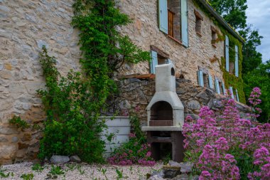 Güzel botanik bahçe bitkiler, renkli çiçekler ve aile ile açık oturma ve barbekü ile arka bahçesinde ile dekore edilmiştir. Alpes-de-Haute-Provence, Fransa'da eski bir evin pitoresk cephesi.