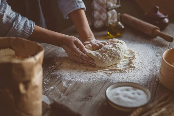 Hands knead the dough for pizza making. Fresh raw dough for pizza or bread baking on wooden board.