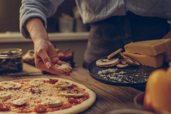 Bir ev hanımı kırsal bir İtalyan mutfağında üsse chees koydu. Akşam yemeği için pizza yapmak, eller ingriduent ekleyin. Ahşap masa üzerinde malzemeler, domates, peynir ve mantar ile pizza yapımı İtalyan gıda.