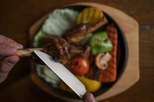 Eating and leisure concept. Dinner on the table. Tasty grilled lamb leg with vegetables and herbs on a roasting iron pan. Assorted delicious vegetables with grilled meat. Toned image. Selective focus.