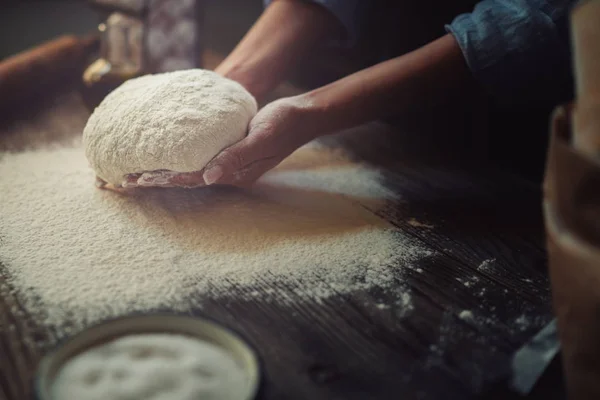 Female hands with dough in ball shape. Basic homemade dough with ingredients on wooden table with natural light. Home healthy food. Low key shot, close up on hands, some ingredients around on table.