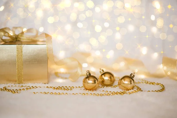 Christmas background with a gold decorations and gift box in snow on the blurred, sparkling background. Toned image with copy space. Selective focus.