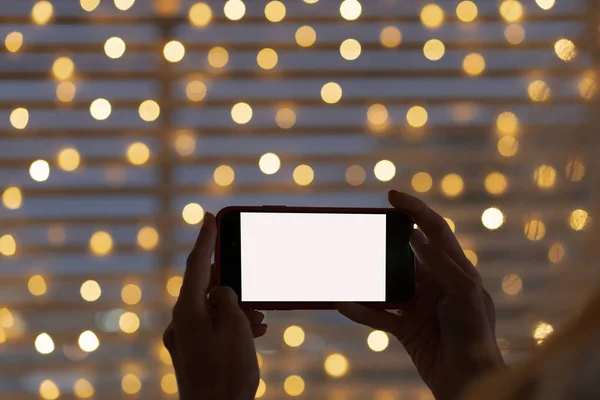 Black mobile phone in woman hand close up. Christmas greeting on phone. Christmas bokeh lights in background.