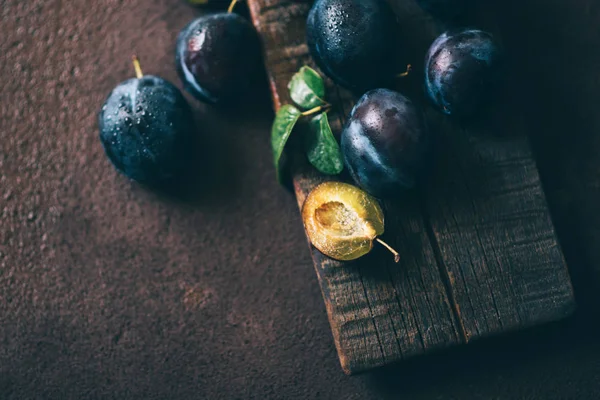 Kahverengi ahşap bir tahta üzerinde yaprakları ile taze olgun erik. Üst görünüm, tonda görüntü. Seçici odaklama.