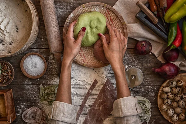 Senior woman cook making tagliatelle pasta with dough in restaurant kitchen. Making pasta. Making pasta in restaurant. Colored raw vegetable pasta with beets, carrots and spinach.