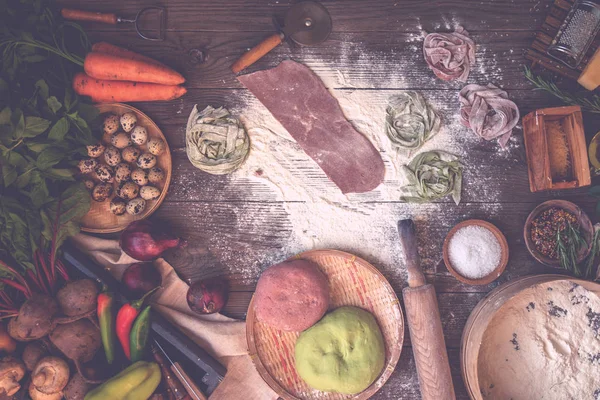 Koyu ahşap masa nın üst görünümünde makarna malzemeleri ile taze ev yapımı makarna. Koyu ahşap bir masa üzerinde İtalyan makarna tagliatelle. Pancar, havuç ve ıspanak ile renkli çiğ sebze makarna.