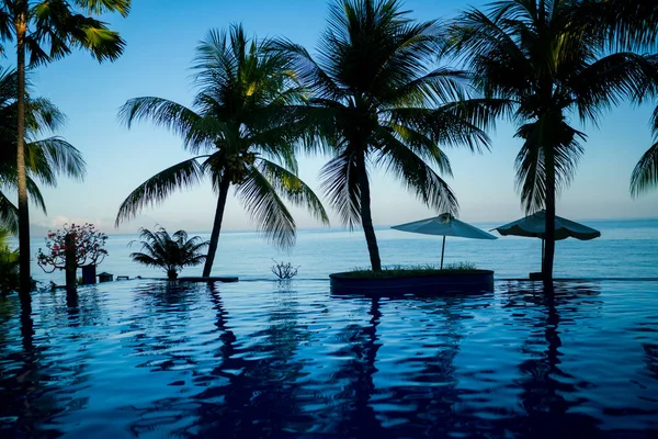 豪华游泳池 热带海岸的海滩 白色的沙滩伞 日光浴床和棕榈树对海 豪华度假村的天然花园 花树和绿色植物 — 图库照片