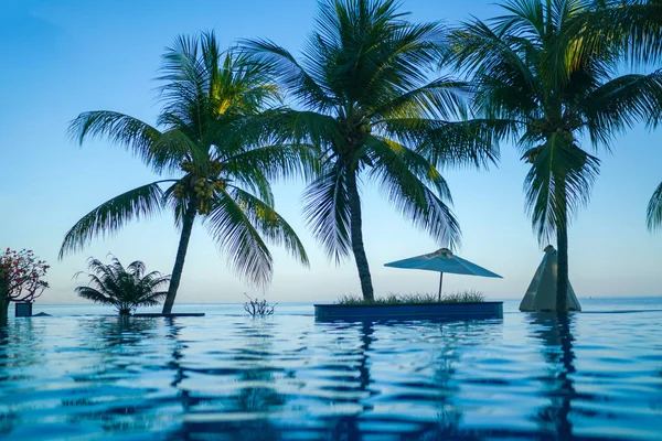 豪华游泳池 热带海岸的海滩 白色的沙滩伞 日光浴床和棕榈树对海 豪华度假村的天然花园 花树和绿色植物 色调图像 — 图库照片