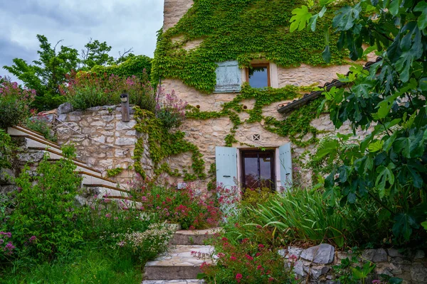 Facade with flowers of old French house. Picturesque typical french rural house decorated with green plants and flowers. Garden with colorful plants in summer season.