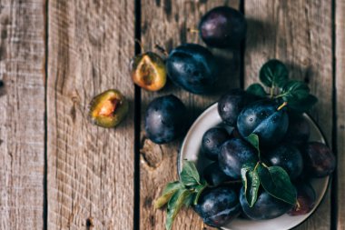 Eski bir ahşap yüzey üzerinde yeşil yapraklı taze mavi erik. Sonbahar hasadı. Sonbahar hasat arka plan. Sağlıklı vejetaryen yemekleri. Biyo, organik yemek. Üst te. Kopyalama alanı.