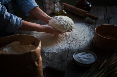 Top şeklinde hamur ile Kadın elleri. Doğal ışık ile ahşap masada malzemelerle temel ev yapımı hamur. Ev sağlıklı gıda. Düşük tuş atış, ellere yakın, masanın etrafında bazı malzemeler.