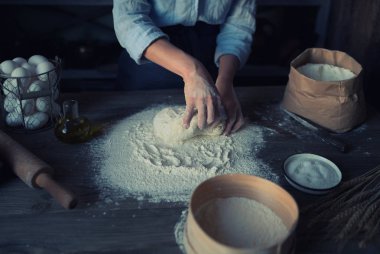 Kadın elleri pizza için hamur yapıyor. Fırıncı mutfak masasında taze çiğ hamur yoğurunuyor. Doğa kavramı, İtalya, gıda, diyet ve biyo. Düşük tuş atış, ellere yakın, masanın etrafında bazı malzemeler.