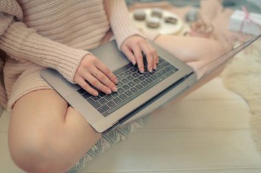 Yumuşak rahat görüntü. Sıcak kazak kız kahve ve kurabiye fincan yanında katta oturan. Bir kızın ellerinin yan görünümü. Kadın sabahın erken saatlerinde kahve içiyor ve dizüstü bilgisayarda e-postaları okuyor. Noel arifesi.