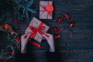 Hediye kutulu kadın elleri. Kırmızı kurdeleli hediye, süslemeler, köknar dalları, kırsal ahşap arka planda kırmızı böğürtlen. Lüks yeni yıl ya da Noel hediyesi. Kış kutlaması. Tonu ayarlanmış resim.