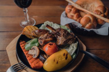 Yemek ve eğlence kavramı. Yemek masada. Sebze ve otlar bir kavurma demir Pan ile lezzetli ızgara kuzu bacak. Çeşitli lezzetli sebze ızgara et ile. Tonlu görüntü. Seçici odak.