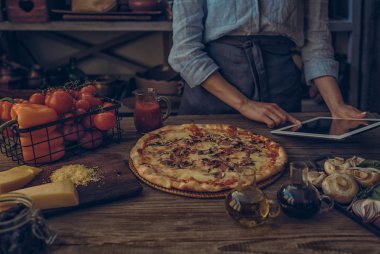 Yemek, yemek, teknoloji ve insan kavramı. Onu mutfakta pizza pişirmek için bir tablet bilgisayar kullanan genç kadın. Bir kadın pecipe yemek ve gıda içerikler pişirmeden önce hazırlanması arama.