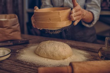 Kadın ekmek ya da pizza için fırında hamur hazırlıyor kırsal bir ahşap yüzeyde doğal ışık altında. Mutfak masasında taze hamurun üzerine un serpiyorum. Seçici odaklanma. Tonu ayarlanmış resim.
