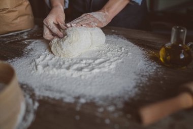 Kadın elleri pizza için hamur yapıyor. Fırıncı mutfak masasında taze çiğ hamur yoğurunuyor. Doğa kavramı, İtalya, gıda, diyet ve biyo. Düşük tuş atış, ellere yakın, masanın etrafında bazı malzemeler.