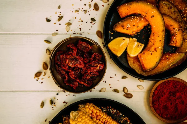 Summer or autumn vegan dinner or snack. Flat-lay of baked pumpkins, grilled sweet corn with smoked sea salt and cilantro over white rustic background, top view. Vegetarian, healthy, alkaline diet concept.