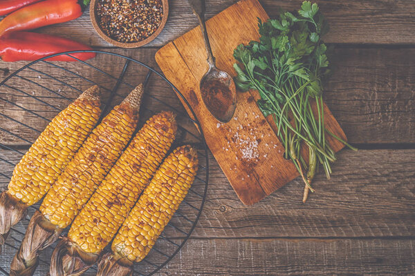 Top view of rustic kitchen table with grilled sweet corn cob with melting butter and vegetables on wooden vintage table. Organic yellow corn ready to eating.