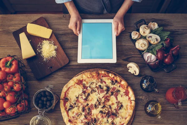 The young woman looking recipe in a tablet computer in kitchen. Healthy food. Healthy lifestyle. Cooking at home. Cooking according to recipe on tablet screen. Technology concept. Toned image.