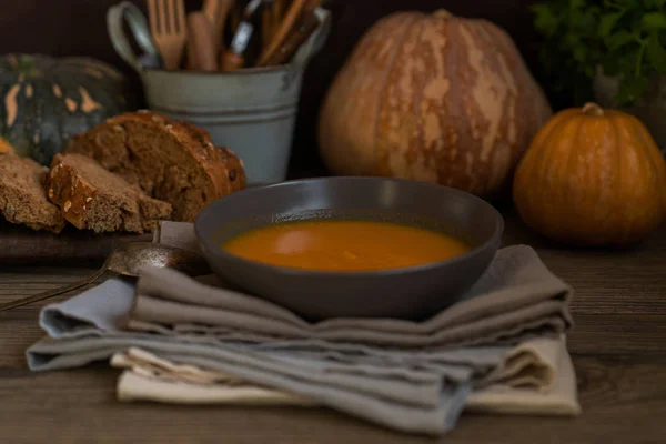 Homemade autumn butternut squash soup with bread. Roasted pumpkin and carrot soup with cream and pumpkin seeds on white wooden background. Concept of healthy eating food. Copy space. Toned image.