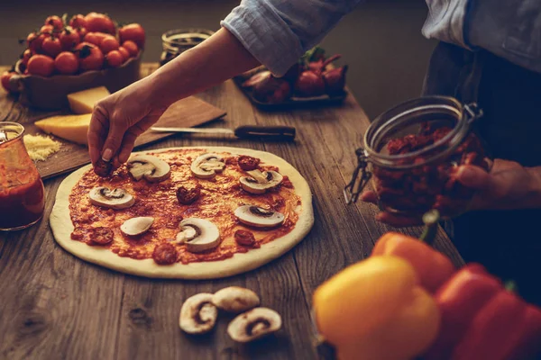 Cook hands. Close up on hands, some ingredients around on table. Fresh original Italian raw pizza, preparation in traditional style. Ingredients and spices for making homemade pizza on wooden table.