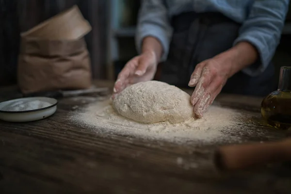 Female hands holding dough in ball shape. Basic homemade dough with ingredients on the side on wooden table with natural light. Home healthy food. Selective focus. Focus on the dough.