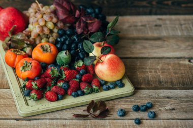 Gökkuşağı meyve arka plan. Çilek, yaban mersini elma, üzüm, hurma, koyu ahşap masa üzerinde nar. Seçici odaklama.