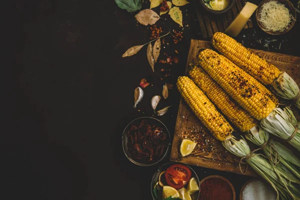 Summer or autumn food background. Ideas for barbecue and grill parties. Grilled corn, cheese on a dark wooden table. Healthy food, organic, bio, homemade food. Copy space, top view.