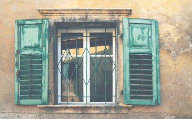 Penceresi olan eski bir retro evin pastel duvarı eski püskü yeşil boyayla boyanmıştır. Eski evin duvarında kepenkleri ve antika camları olan yeşil ahşap bir pencere, klasik bir bina. Tonu ayarlanmış resim.