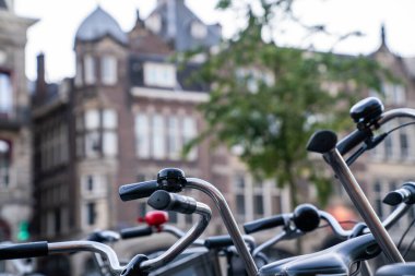 Avrupa 'da şehir merkezinde bisiklet gidonları ve çanların yakın plan çekimleri, arka planda bulanık tarihi mimari, Avrupa sokaklarının kentsel bisiklet kültürü ve cazibesini yakalıyor.