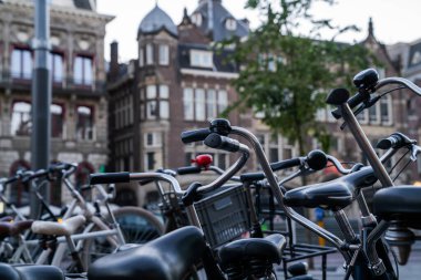 Avrupa 'da şehir merkezinde bisiklet gidonları ve çanların yakın plan çekimleri, arka planda bulanık tarihi mimari, Avrupa sokaklarının kentsel bisiklet kültürü ve cazibesini yakalıyor.