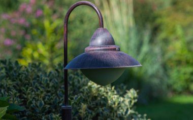 Yumuşak, doğal ışıklandırması ve arka planında bitkiler olan yemyeşil bir arazide eski tip bahçe feneri barışçıl ve sakin bir açık hava ortamı yaratıyor..