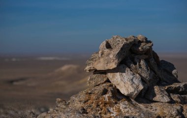 Issız bir arazide ıssız bir kaya oluşumu berrak bir gökyüzünün altındaki uzak tepeler çölün katıksız güzelliğini ve jeolojik özelliklerini gözler önüne seriyor.