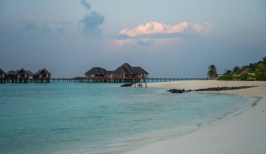 Yumuşak beyaz kumlu ve kristal berrak turkuaz su ile tropik plaj maldivler, su bungalovları üzerinde, denizde ahşap salıncak, uzun bir iskele ve sazlı çatı restoranı