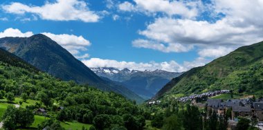 Çiçekli, yeşil bir vadinin panoramik manzarası. Geleneksel evler, mavi gökyüzünün altındaki yüksek dağların eteklerinde. Kabarık bulutlar..