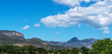 İspanya 'nın Pireneler bölgesindeki pitoresk bir manzarada, kayan tepeler ve gür ormanlar arasında yuva yapmış bir köy yer alıyor. Açık mavi gökyüzü tüylü bulutlarla doludur. Engebeli dağların manzarası..